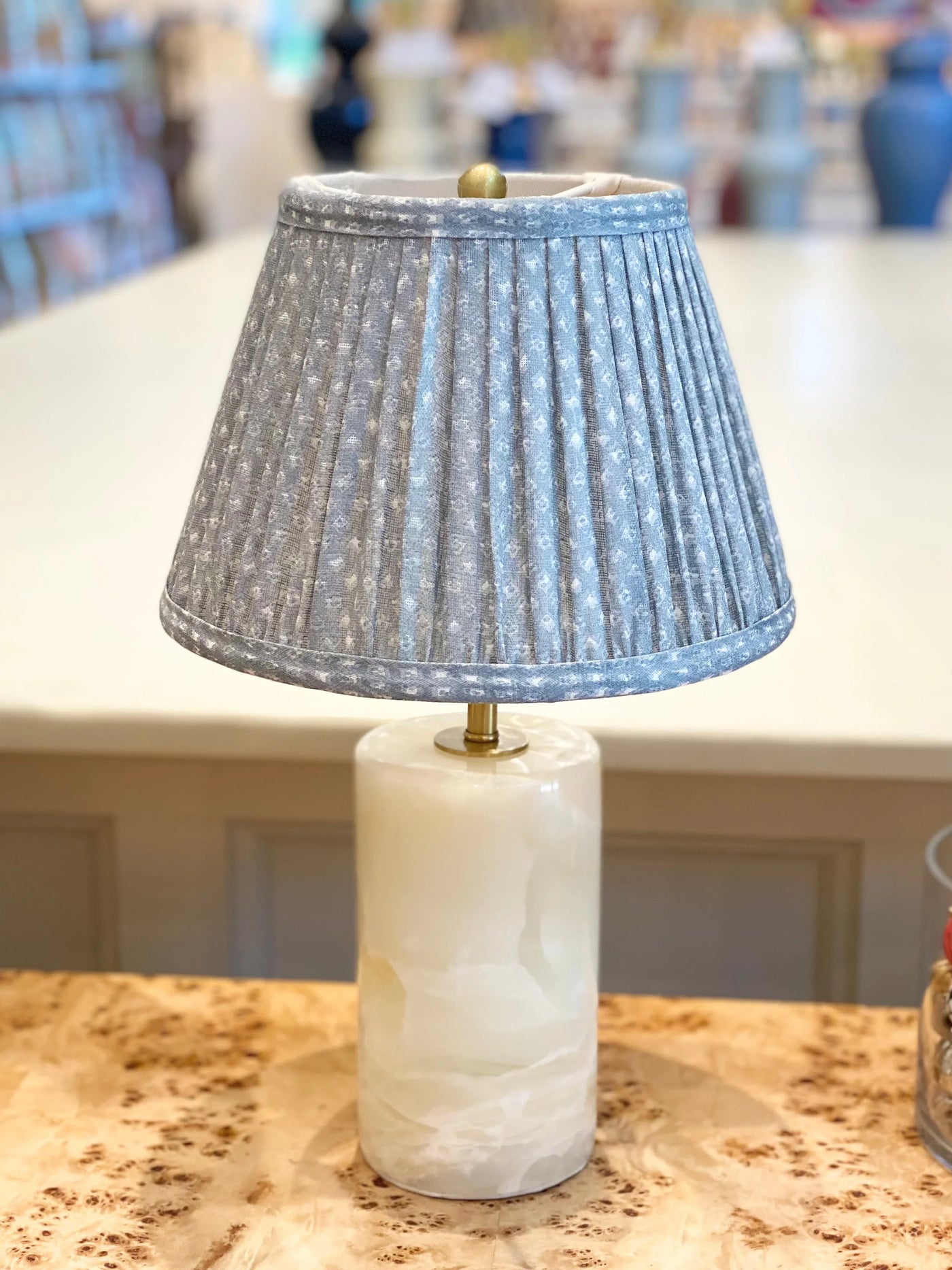 Fermoie blue figured pleated lampshade displayed on an alabaster lamp base, combining soft floral patterns and luxurious materials for an elegant look.