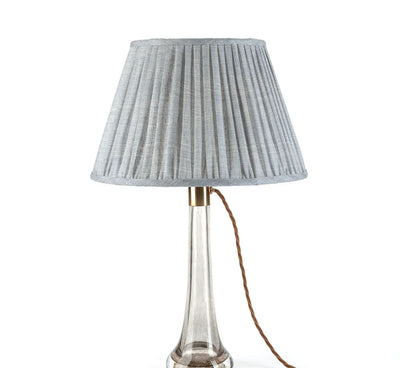 Luxury designer Fermoie Blue Moire gathered empire lampshade with pleated detailing displayed on a clear glass lamp base.