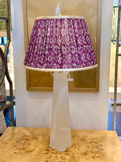 Alabaster table lamp with purple patterned pleated lamp shade on wood surface