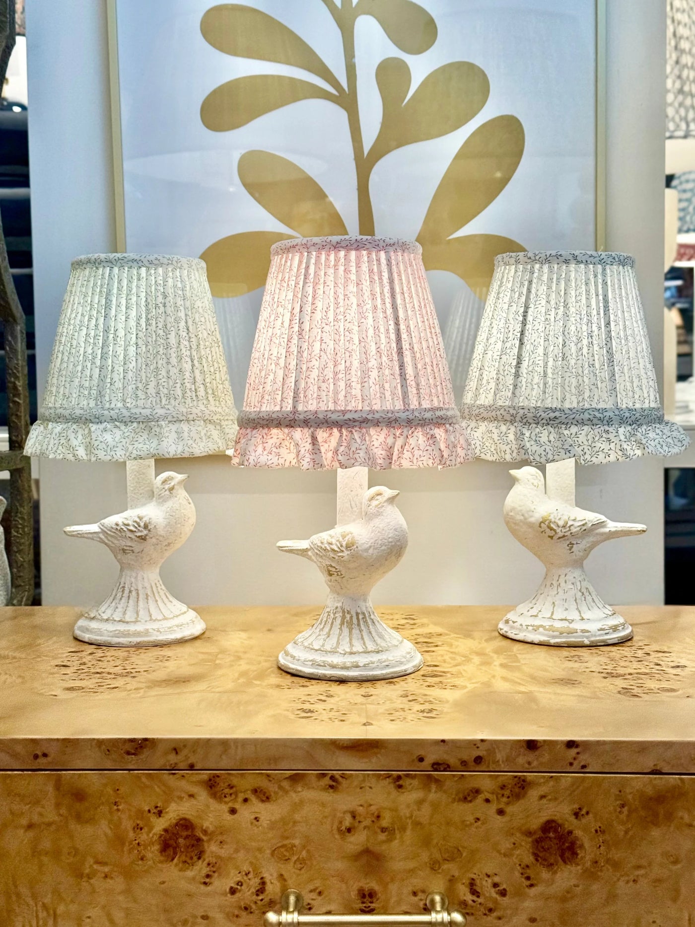Three decorative lamps with bird bases on a wooden surface, against a decorative wall.