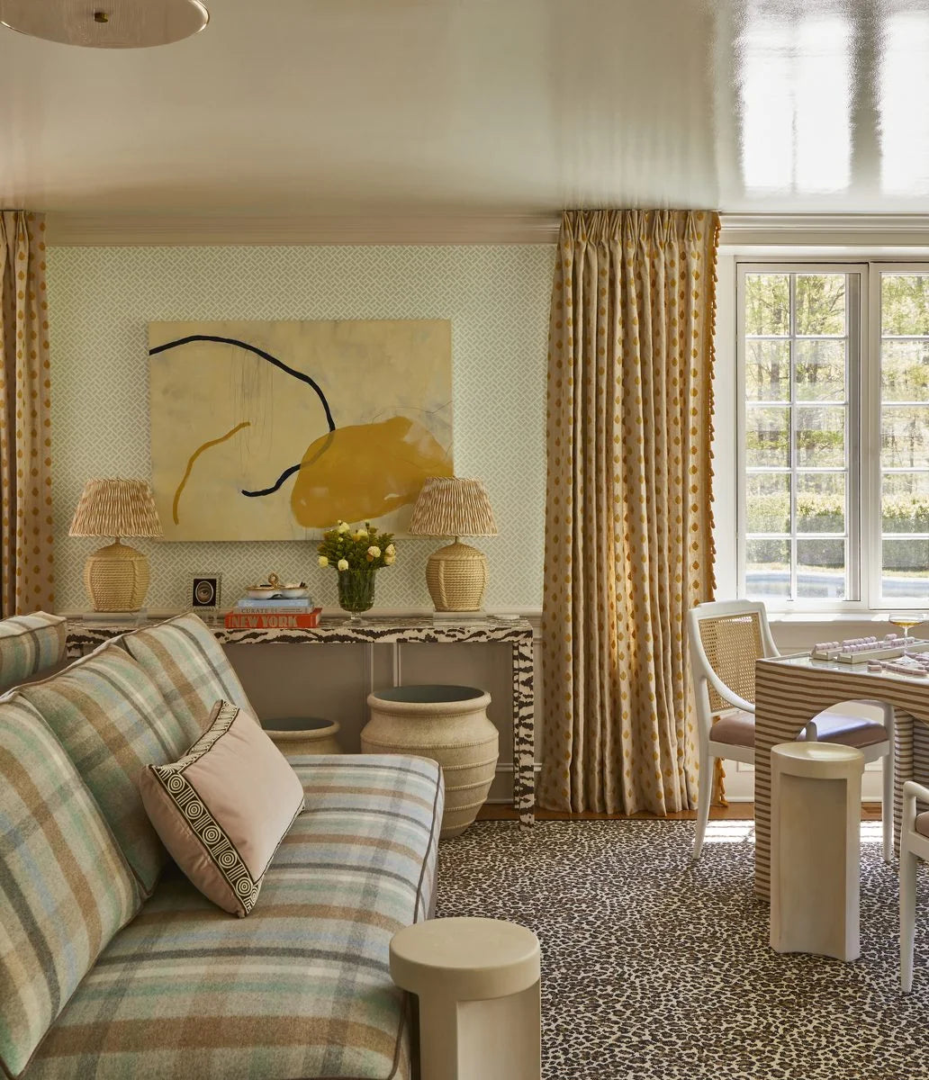 Pleated Ian Sanderson Honey Quiver lampshades on rattan lamps beside plaid upholstery and a spotted rug in Toledo Geller’s game room.