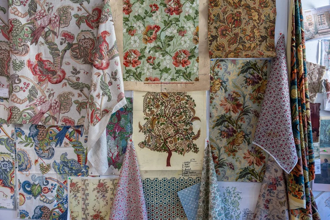Lengths of floral printed fabric hang across the studio wall beside pinned references