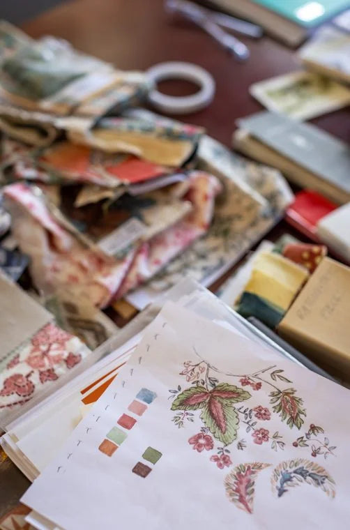 A desk covered with fabric scraps, drawings, and a color chart