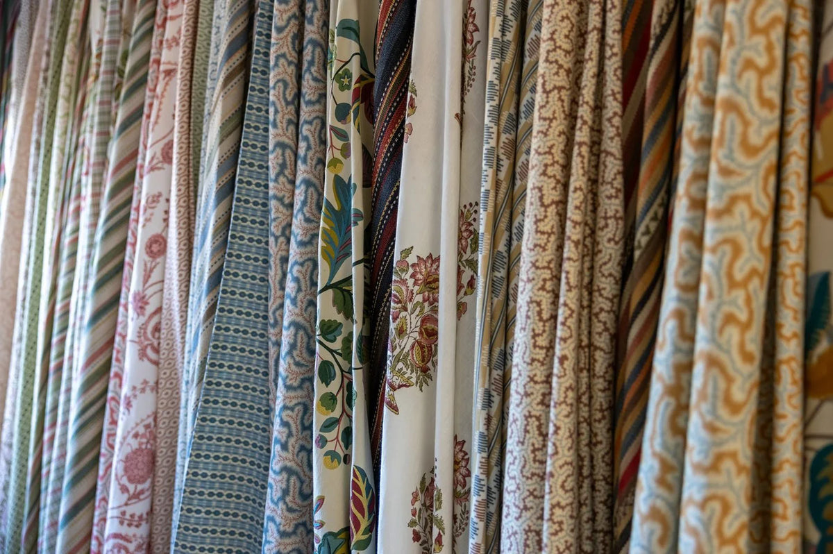 Lengths of striped, checked, and printed fabric hang side by side in the studio