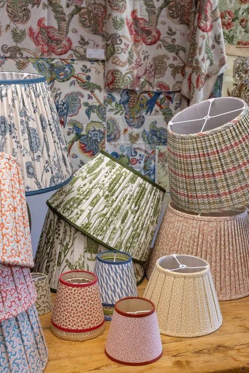 A gathered plaid lampshade leans against a pleated striped one on the table
