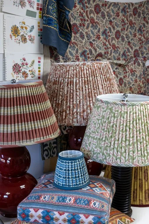 A striped lampshade on a red gourd lamp beside a small pleated lampshade on a patterned box