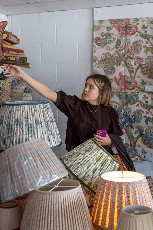 A member of The Shade Shop team reaches for a lampshade among the pleated lampshades in the studio